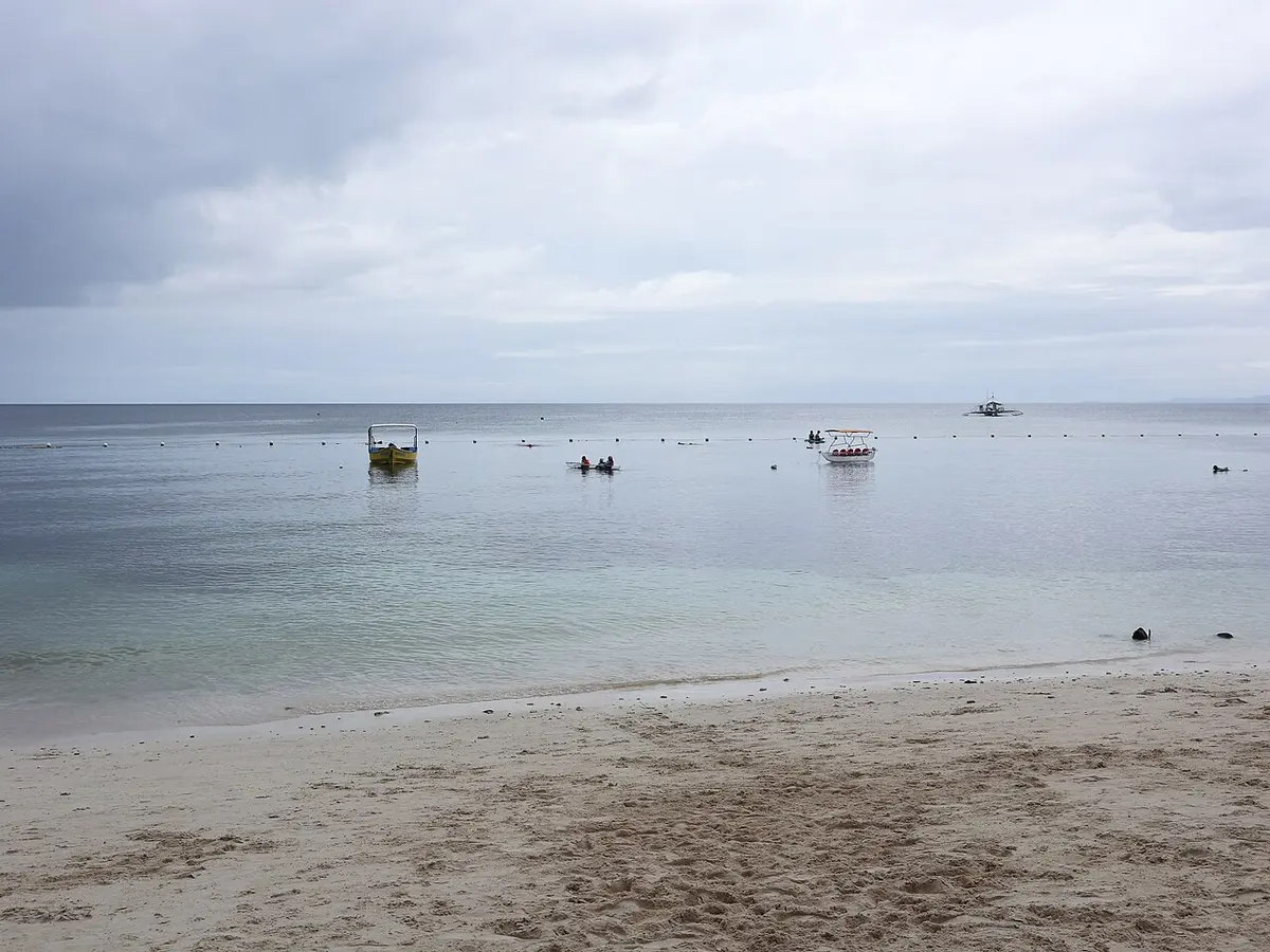 Calm water and sand under an overcast sky along the Alona Beach seafront on Panglao Island.