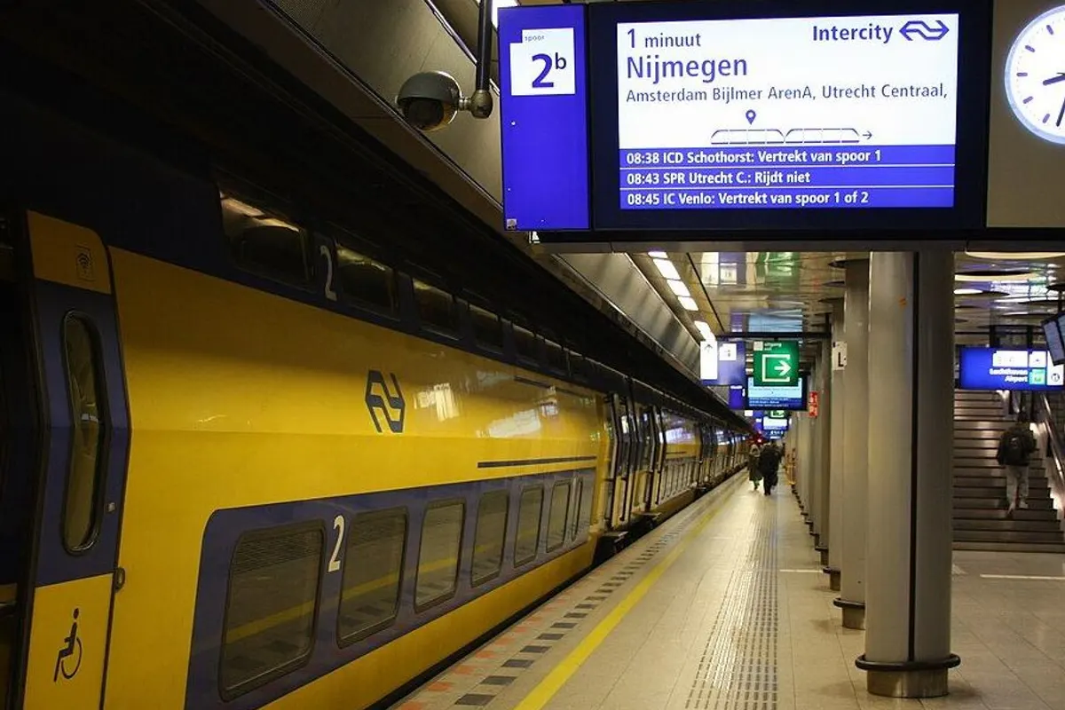 A yellow double-deck NS train at the underground platform, with the departure board above.