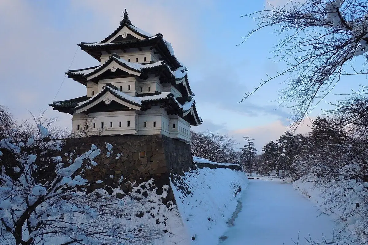 The three-tier keep of Hirosaki Castle above a snow-covered stone wall and moat.
