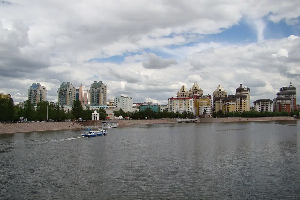 The wide Ishim River in Astana under a cloudy sky, with a riverside promenade and apartment blocks beyond.