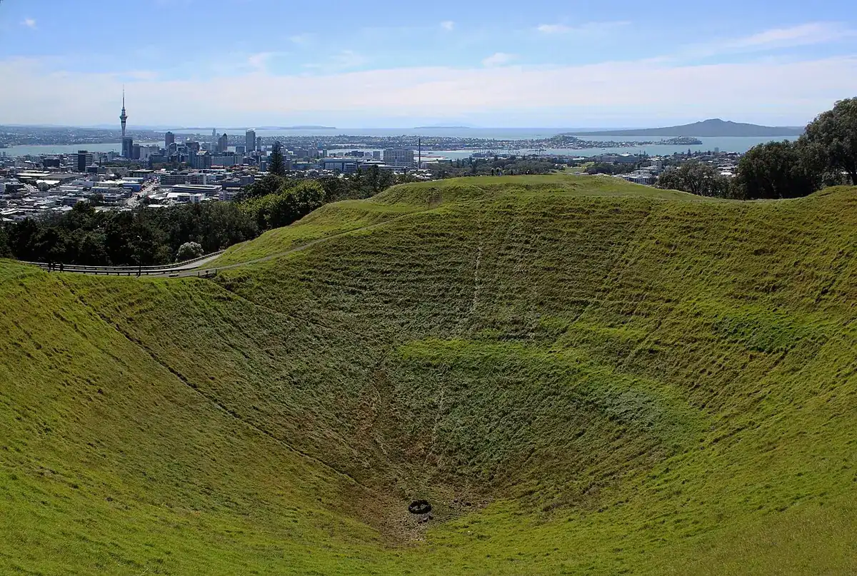 The grassy Mt Eden crater with Auckland's city centre and Rangitoto Island beyond