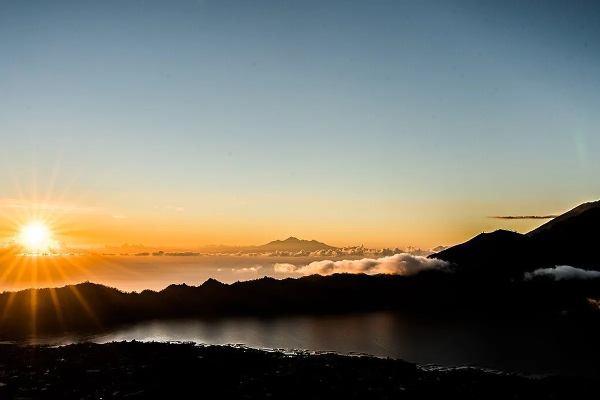 Sunrise seen from Mount Batur, with Lake Batur below and a distant peak rising above the clouds.