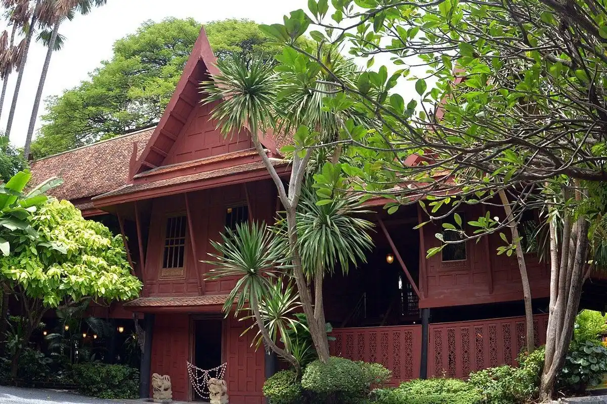 The red teak traditional Thai house seen through the trees of its tropical garden.