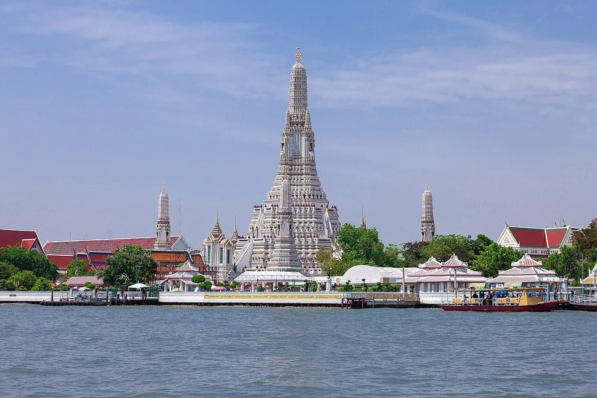 Wat Arun's white central prang in daylight, seen across the Chao Phraya River.