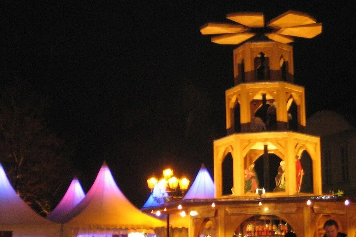 An illuminated wooden Christmas pyramid and colourful tents under the night sky.