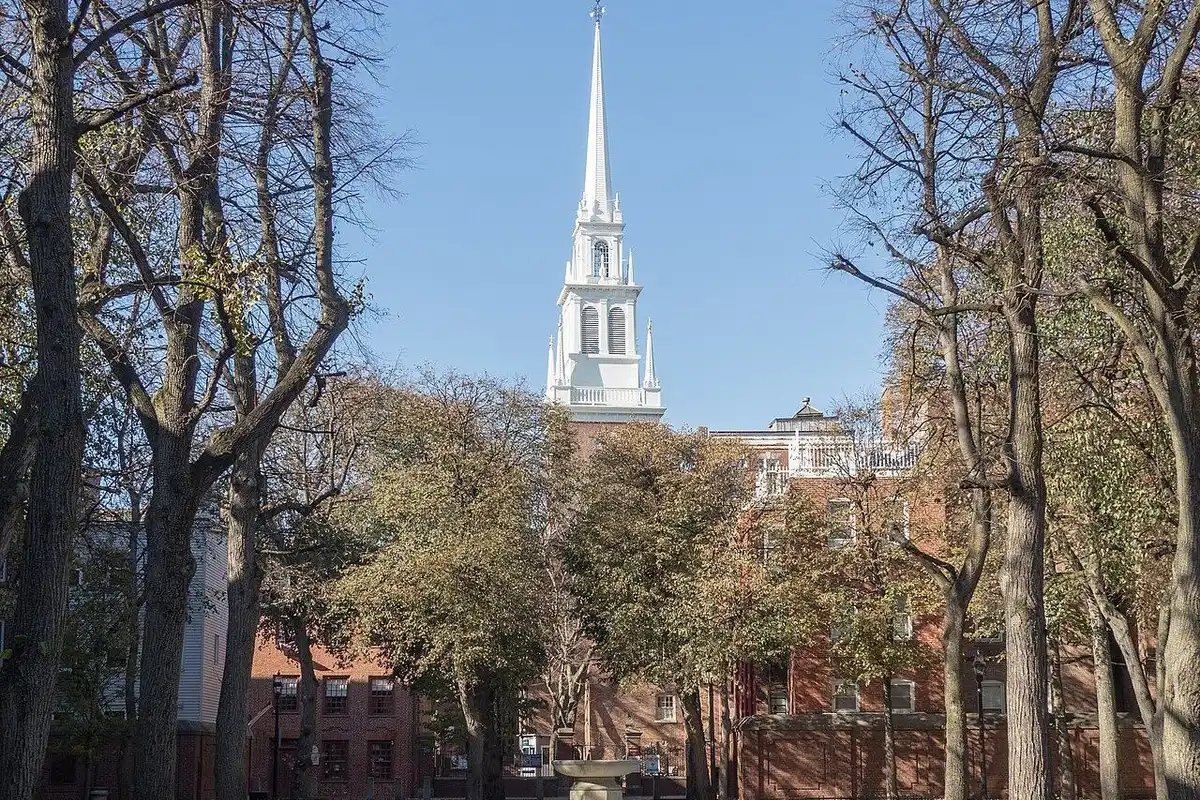 The white steeple of Old North Church rising above the trees of Paul Revere Mall, with a fountain in the foreground.