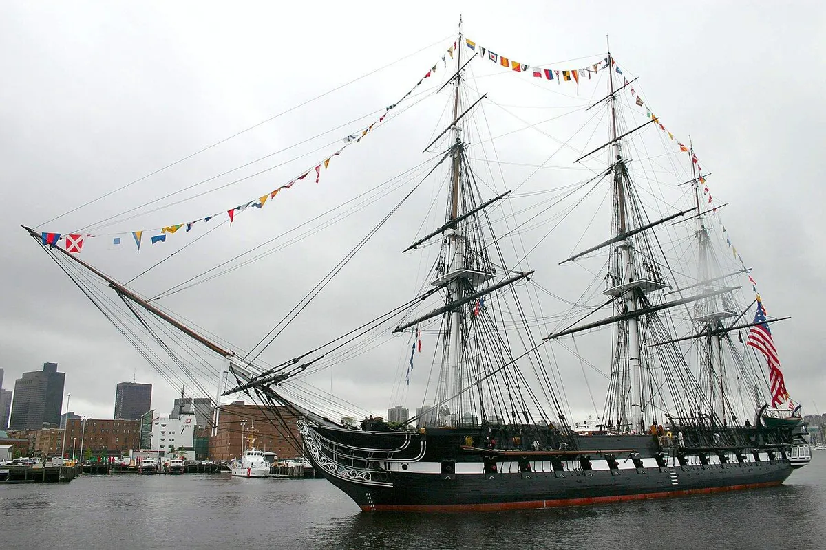 USS Constitution, a three-masted sailing frigate dressed with signal flags, afloat in Boston Harbor.