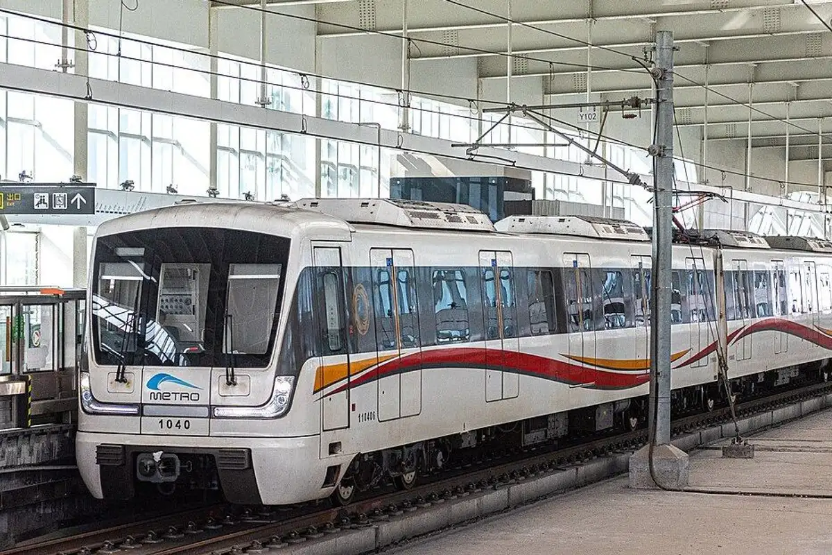A white Line 10 train with red stripes pulling into a covered elevated station.