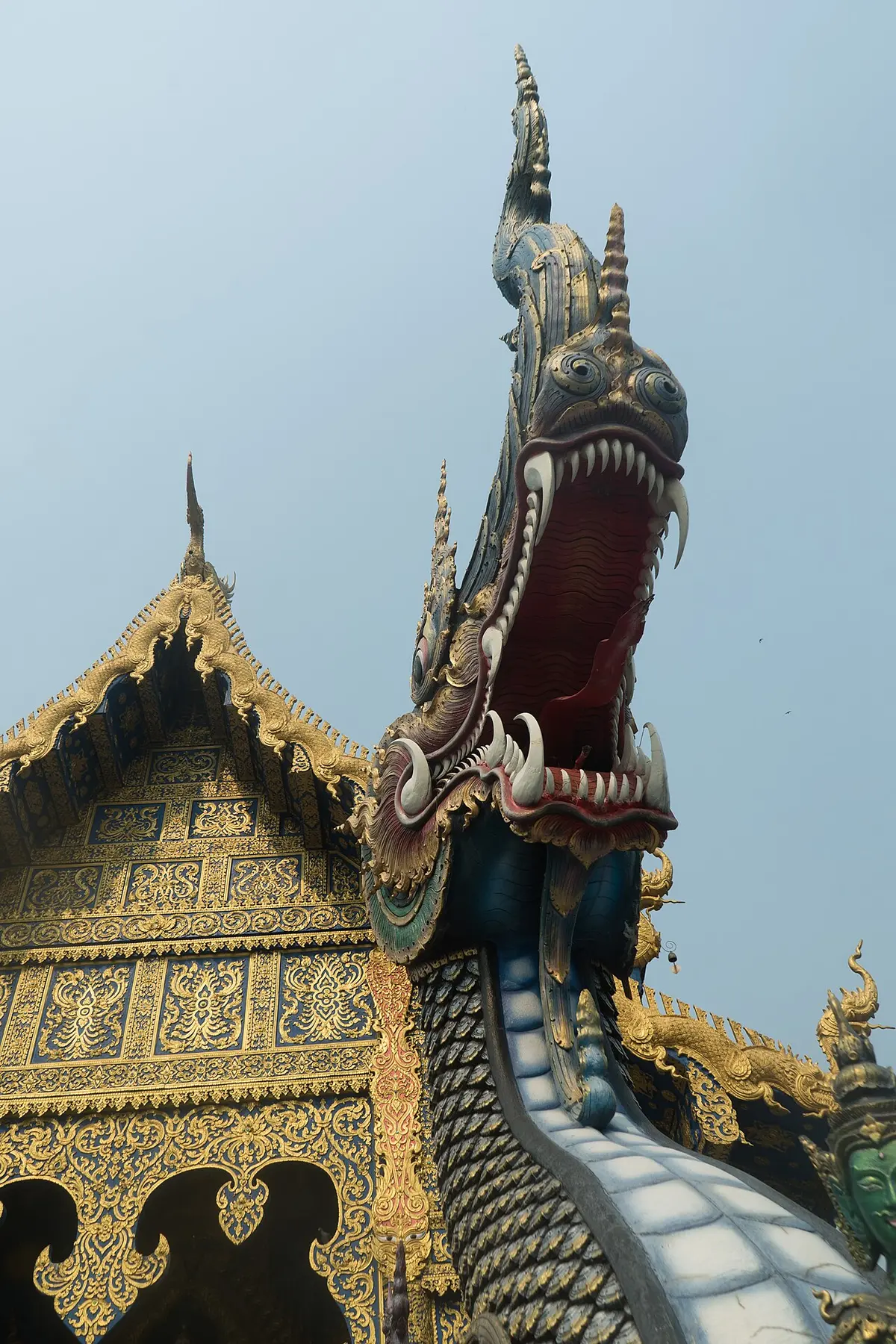A blue naga sculpture with gold details beside the temple roof