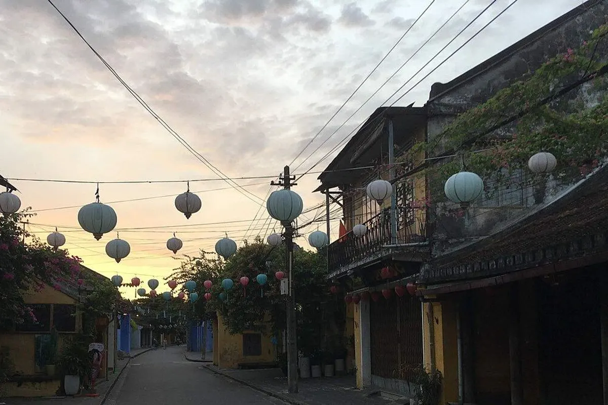Lanterns strung over a quiet Hoi An Old Town street lined with old yellow houses at sunrise.