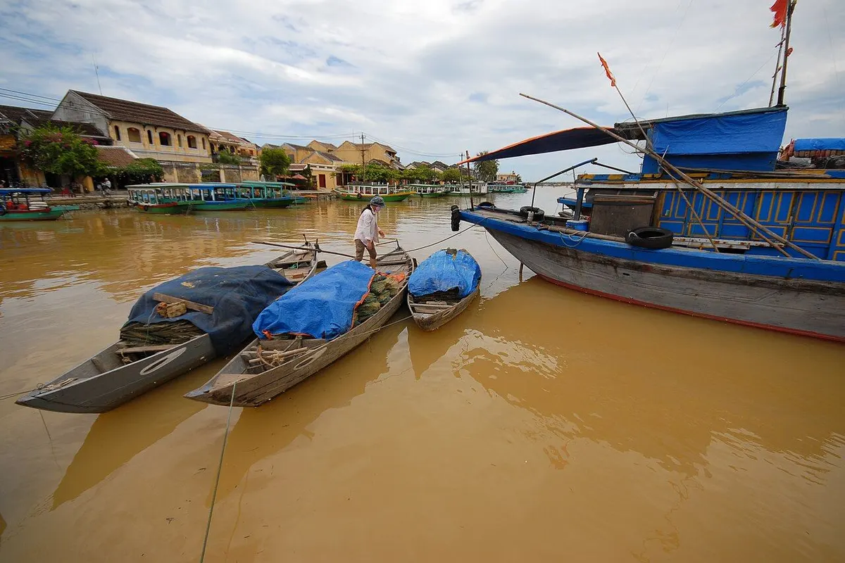 Wooden fishing boats moored on the river in front of the old yellow houses of Hoi An.