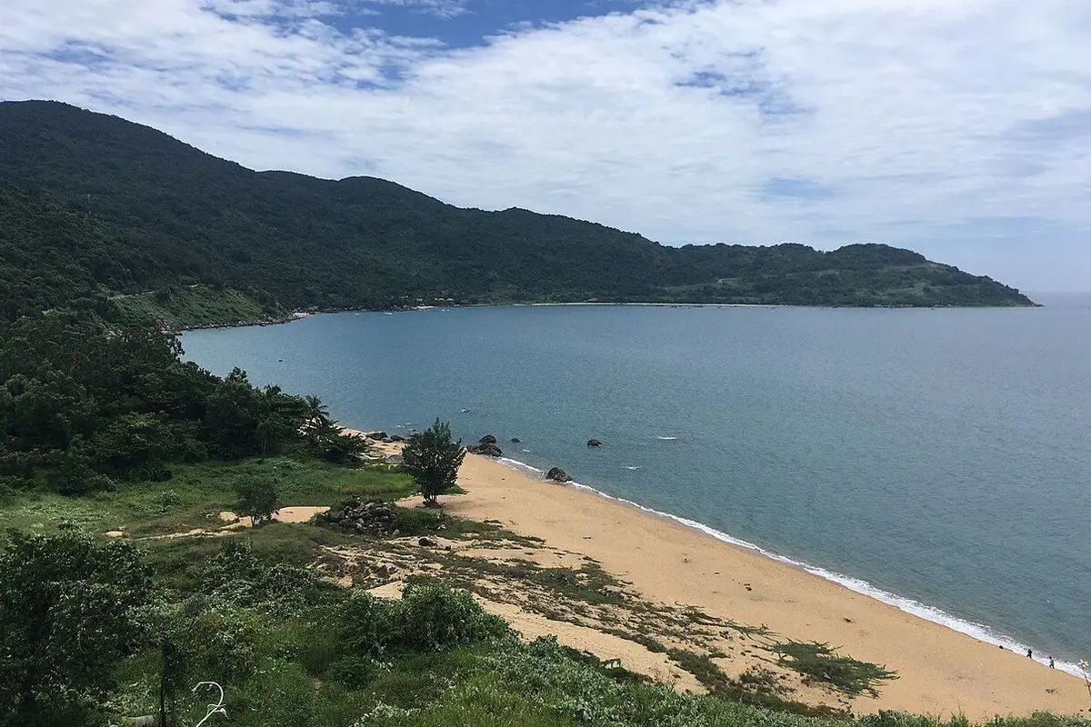 A sandy beach and calm bay below the forested ridge of the Son Tra Peninsula.