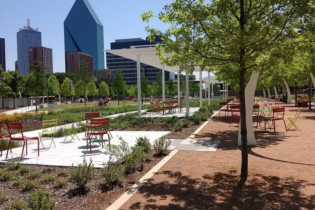 Shaded walkways and a plaza with red and lime-green chairs on the east side of Klyde Warren Park.