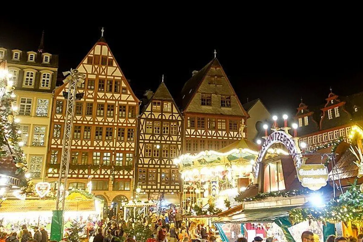 Half-timbered houses, a carousel and stalls lit up at night on the Römerberg.