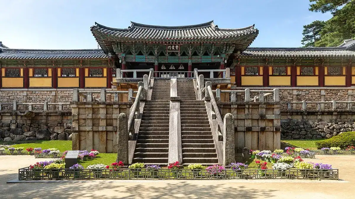 The Cheongungyo and Baegungyo stone stairways and halls of Bulguksa Temple behind a flower bed under a blue sky.