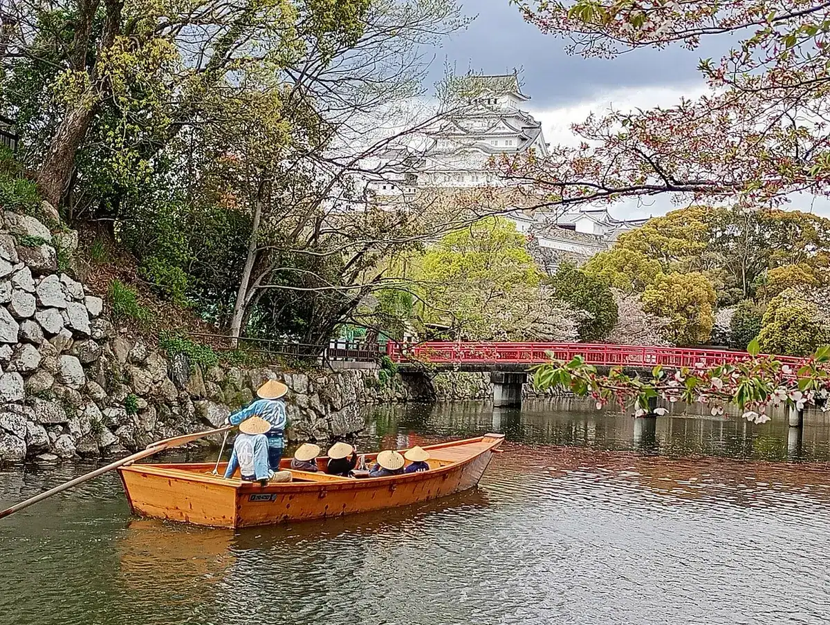 Himeji Castle's keep seen across the moat with cherry blossoms and a small wooden boat.