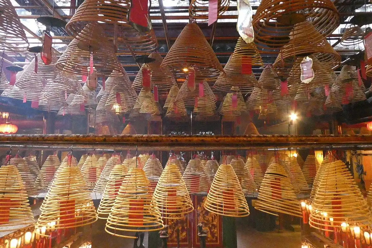 Rows of cone-shaped incense coils with red paper tags hang beneath the temple roof.