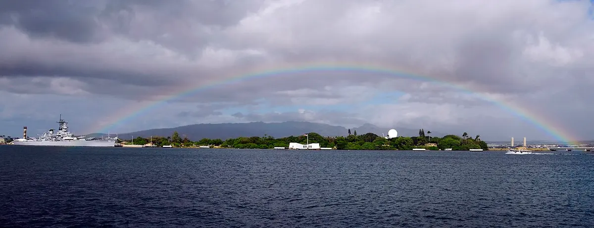 The white USS Arizona Memorial on Pearl Harbor beneath a rainbow