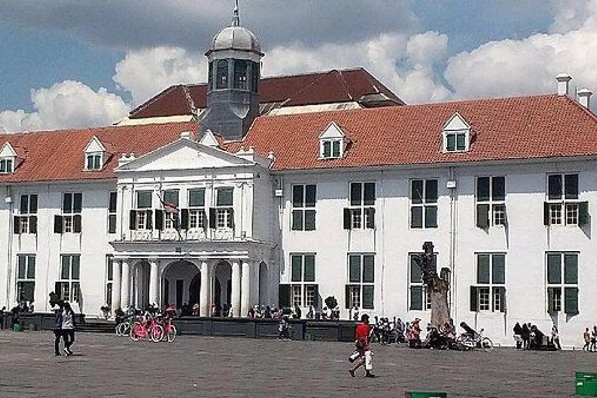Fatahillah Square in Kota Tua with the white, red-roofed former city hall (Jakarta History Museum) under a blue sky with white clouds.