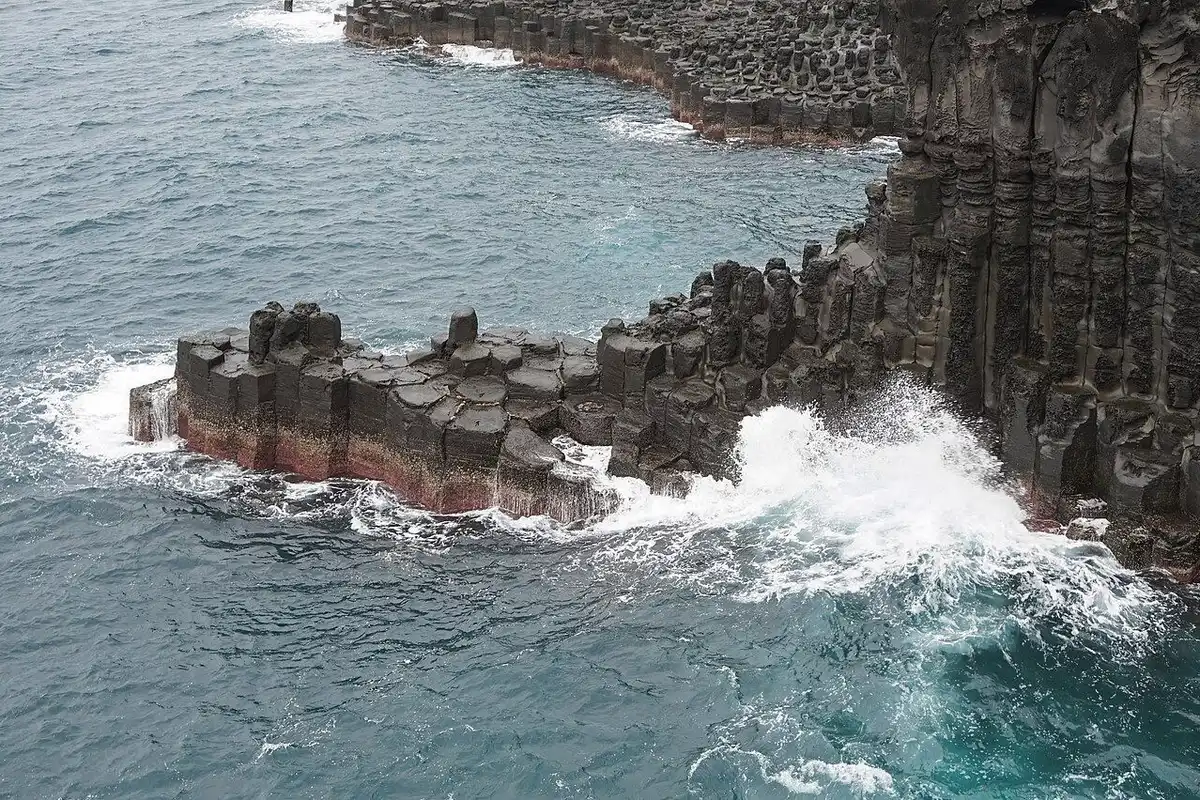 Waves break white against tightly packed hexagonal basalt columns on the Daepo Jusangjeolli coast.