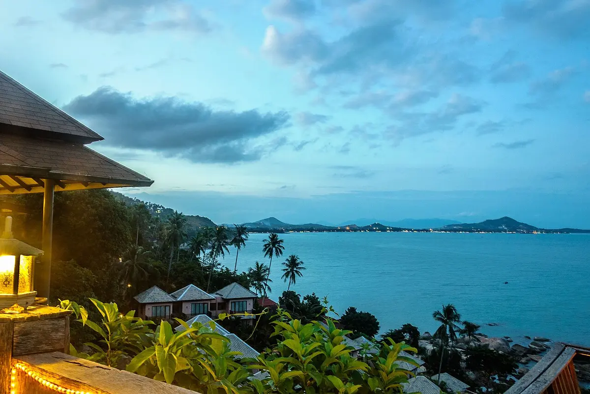 Palm trees and forest above a blue bay at dusk, with distant islands