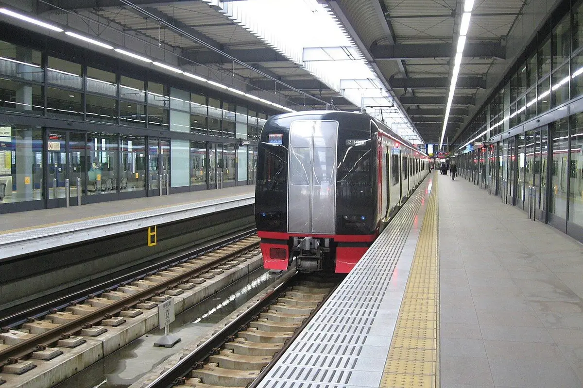 A red-and-black Meitetsu limited express train at the end of a wide airport station platform.