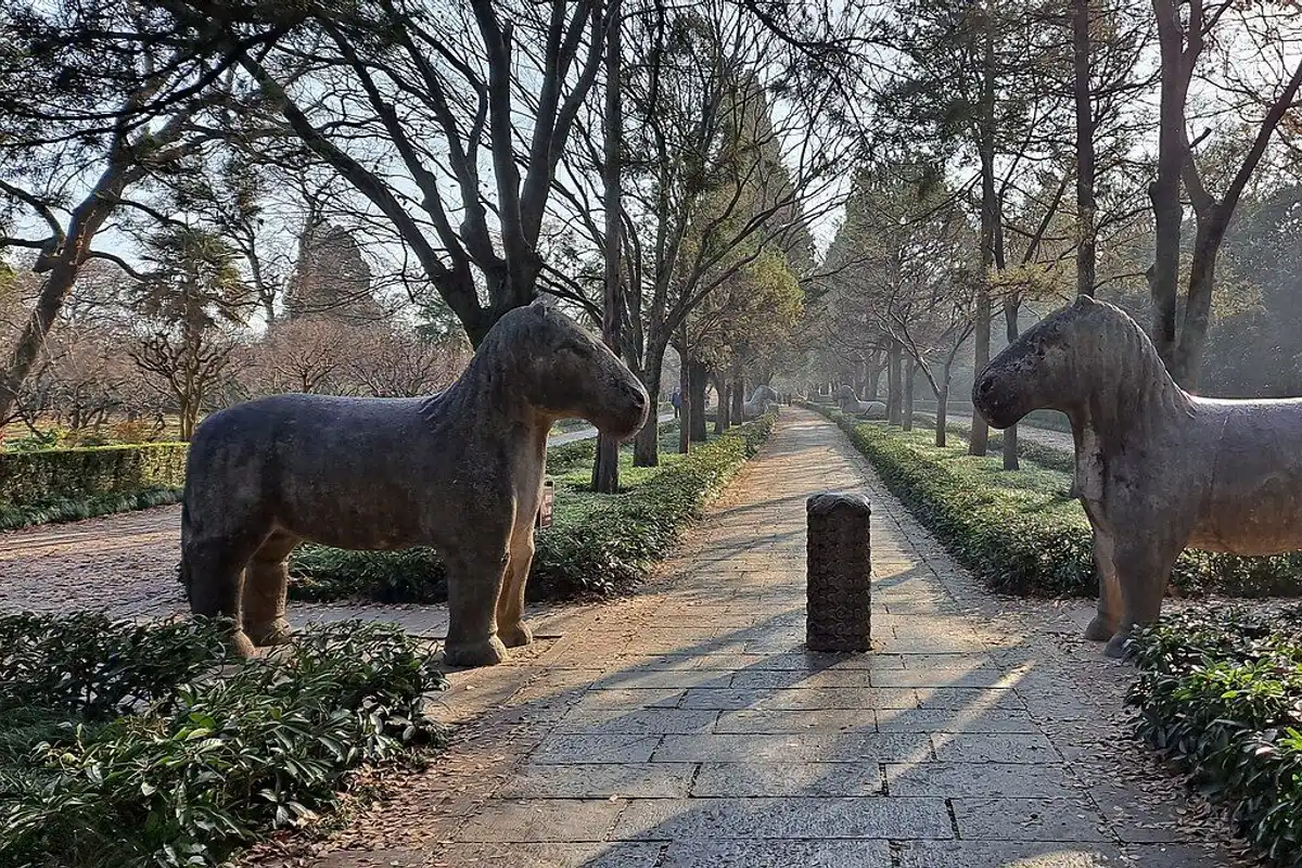 A pair of stone horses facing each other on either side of a tree-lined path.