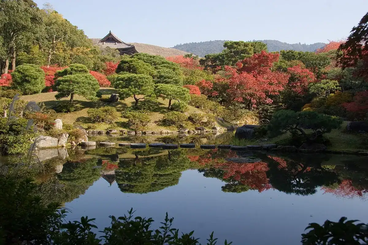 Isuien's pond garden in autumn colors, with the roof of Todai-ji's Nandaimon gate beyond.