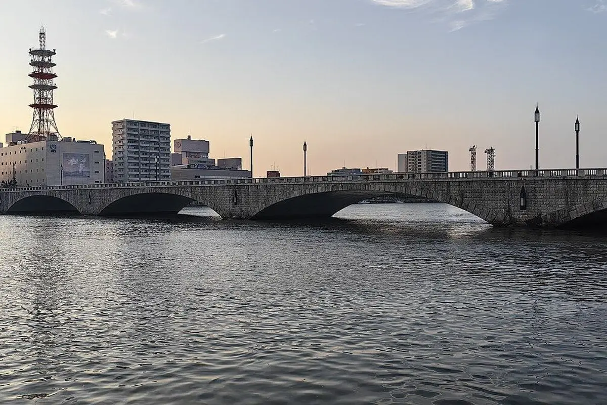 The stone arches of Bandai Bridge over the Shinano River at dusk, with the city behind.