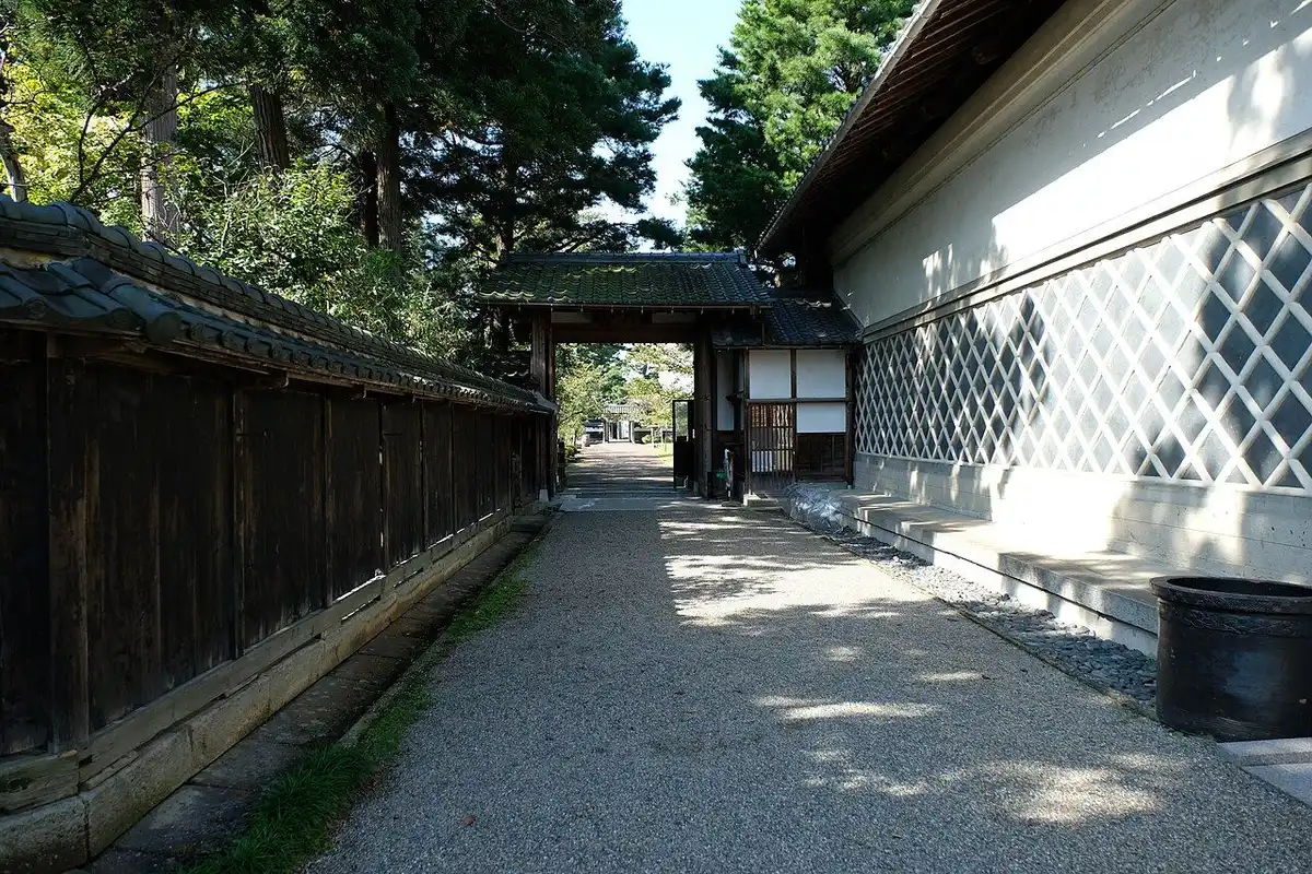 A gravel path running between a tiled black wooden fence and a white storehouse wall with a diamond pattern to a gate at the Northern Culture Museum.