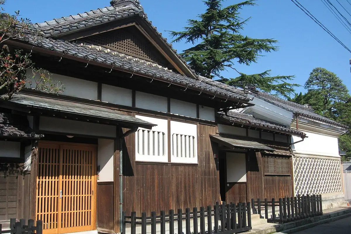 The entrance side of the old villa, with tiled roofs, dark timber walls and a wooden lattice door.