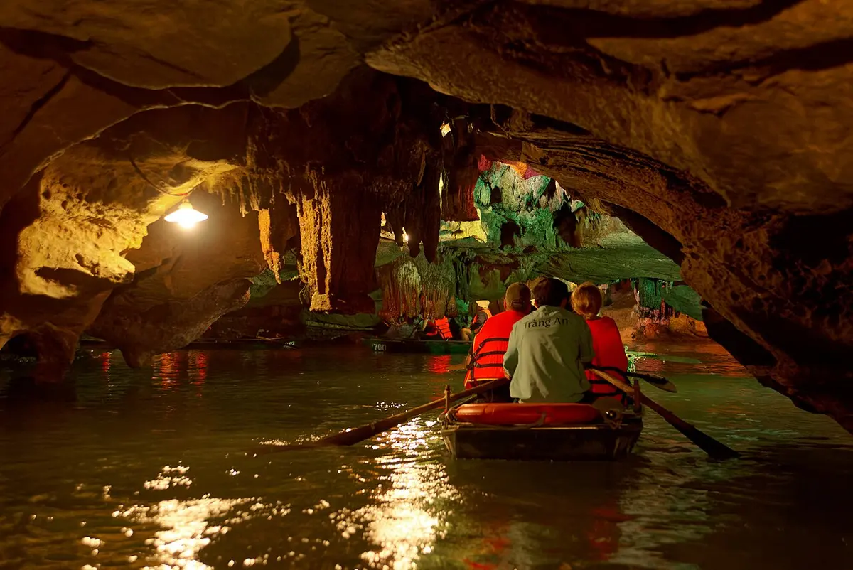 A tour boat gliding through a lit limestone cave at Trang An