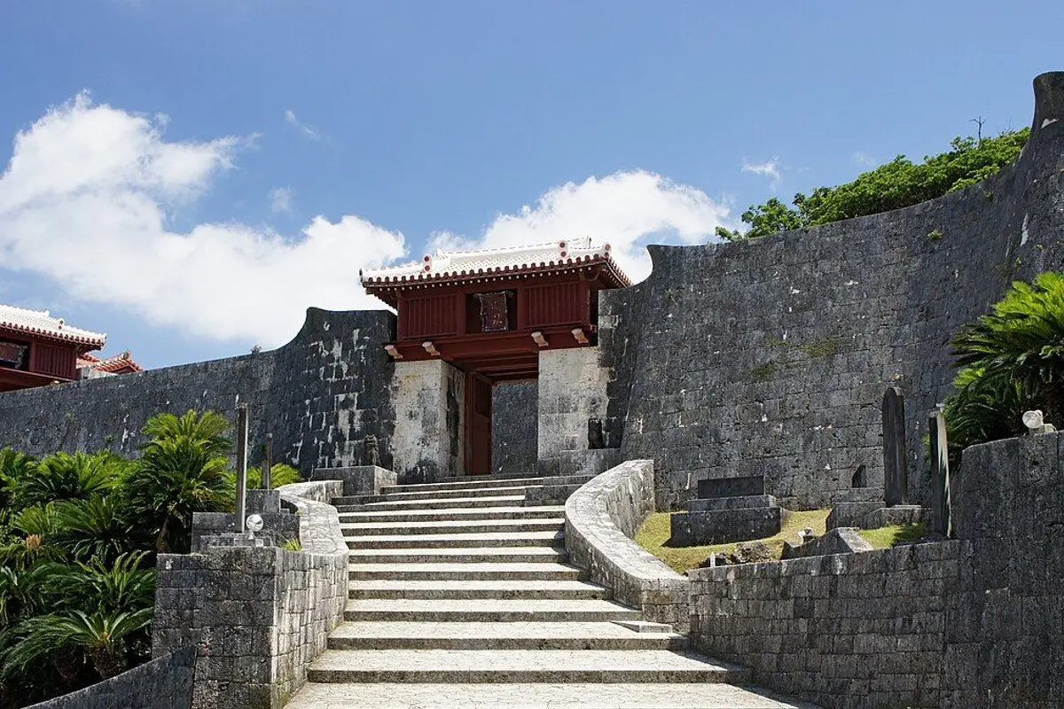 Stone stairs leading up to Zuisenmon, a red-roofed gate set in the curving stone walls of Shuri Castle.