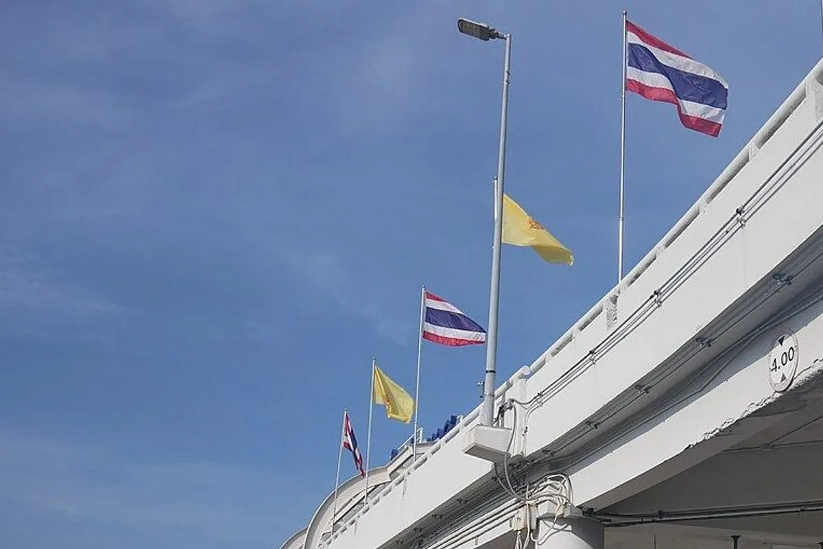 Flags flying along the elevated roadway in front of the Phuket airport terminal under a blue sky.