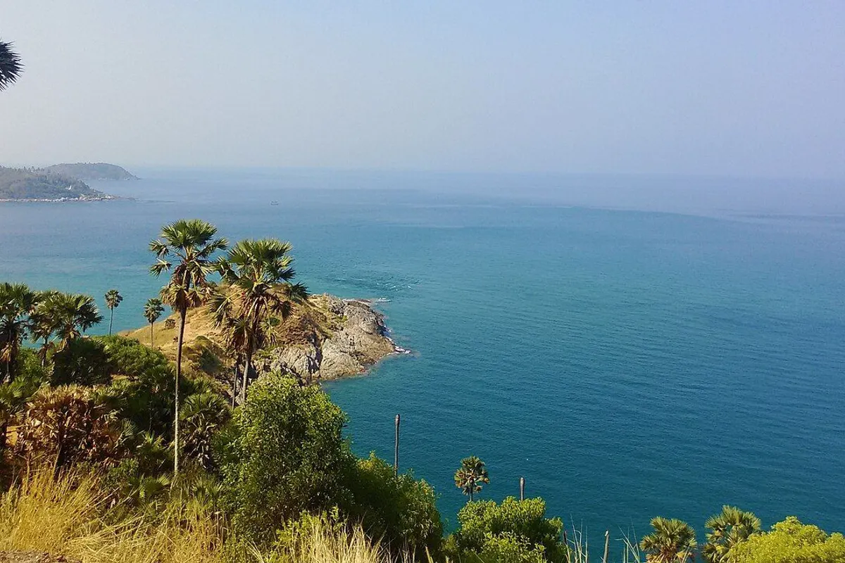 Promthep Cape reaching into the calm Andaman Sea beyond sugar palms, with an island on the horizon.
