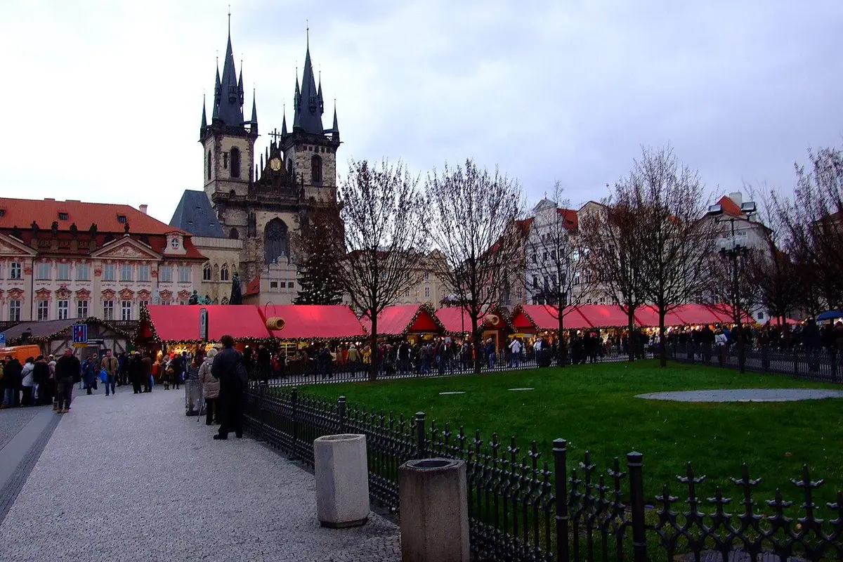 Red-roofed stalls lined up on Old Town Square below the Týn Church in the afternoon.