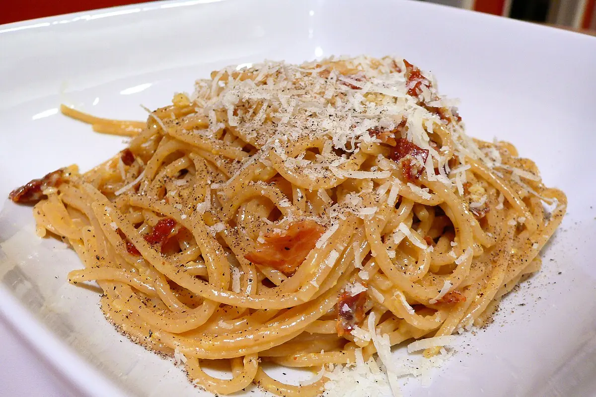 A plate of spaghetti carbonara topped with grated cheese and black pepper