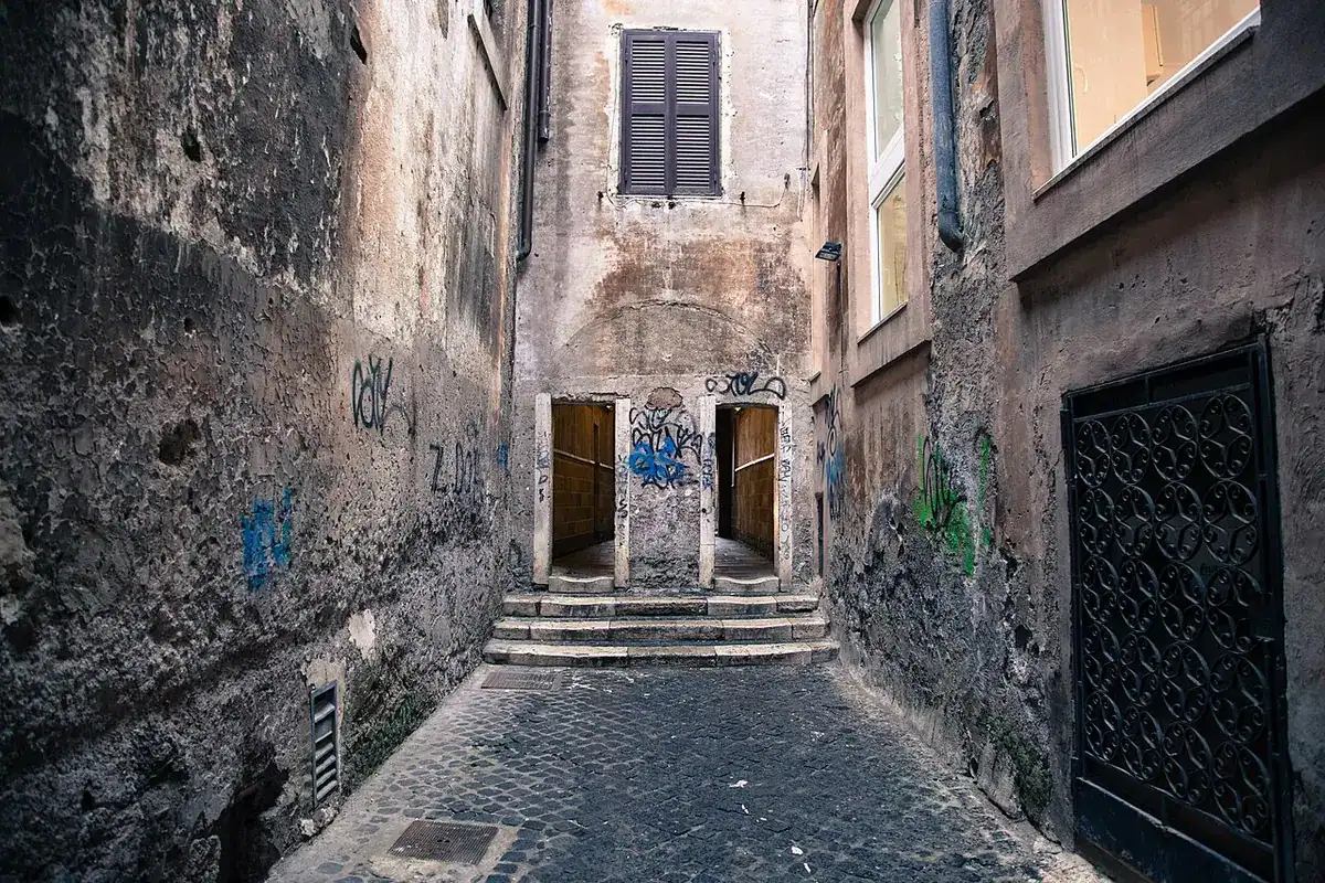 A narrow cobbled alley with steps and weathered walls in Rome