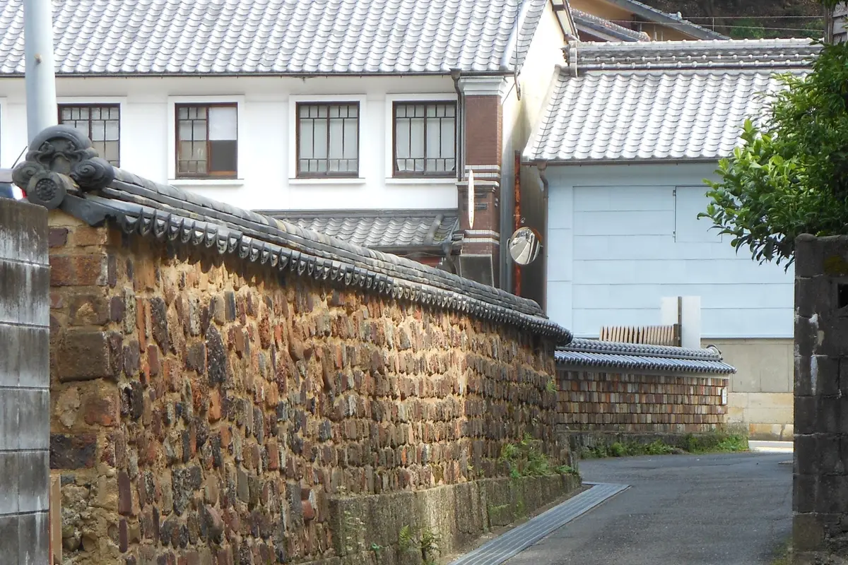 A tile-capped wall built from old kiln bricks runs along a narrow lane in Arita's Uchiyama district, with white-walled tiled houses behind.