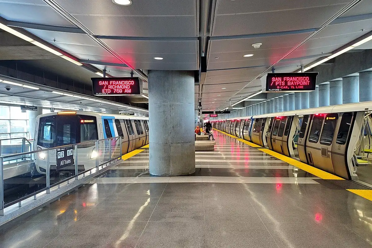 BART trains standing on both sides of the platform beneath destination displays.