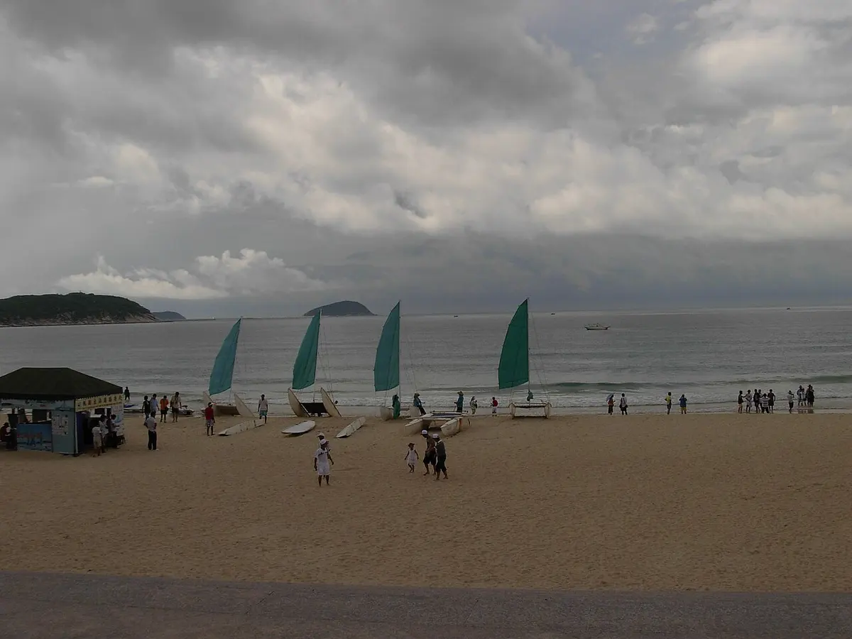 Sailboats off the wide sandy beach of Yalong Bay under a cloudy sky