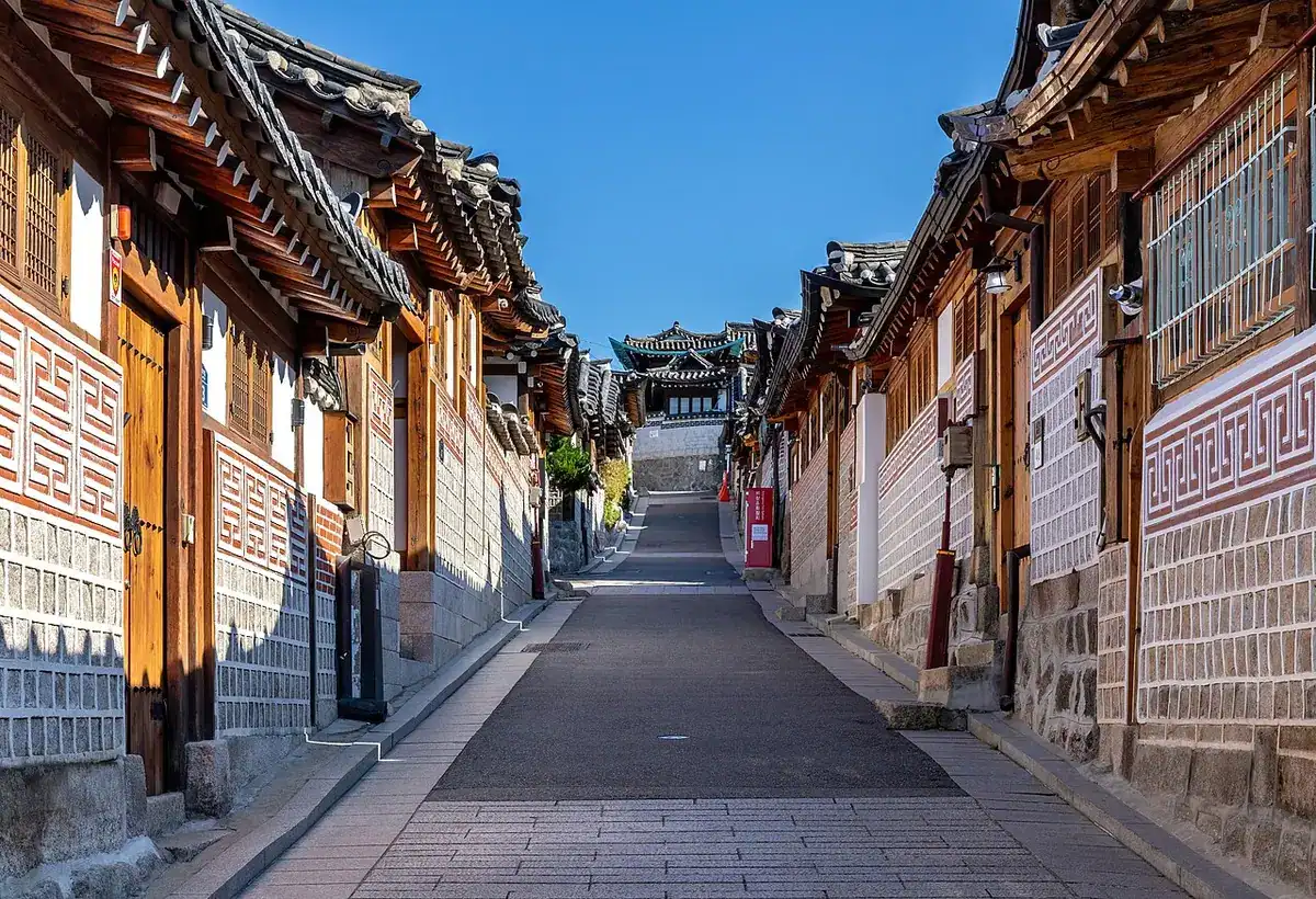 A Bukchon lane lined with tiled hanok roofs under a blue sky