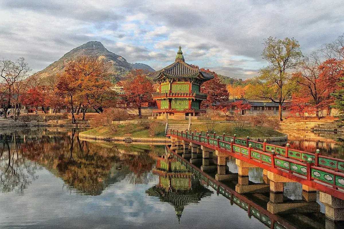 Gyeongbokgung's Hyangwonjeong Pavilion reflected in its pond among autumn trees, with Bugaksan behind.