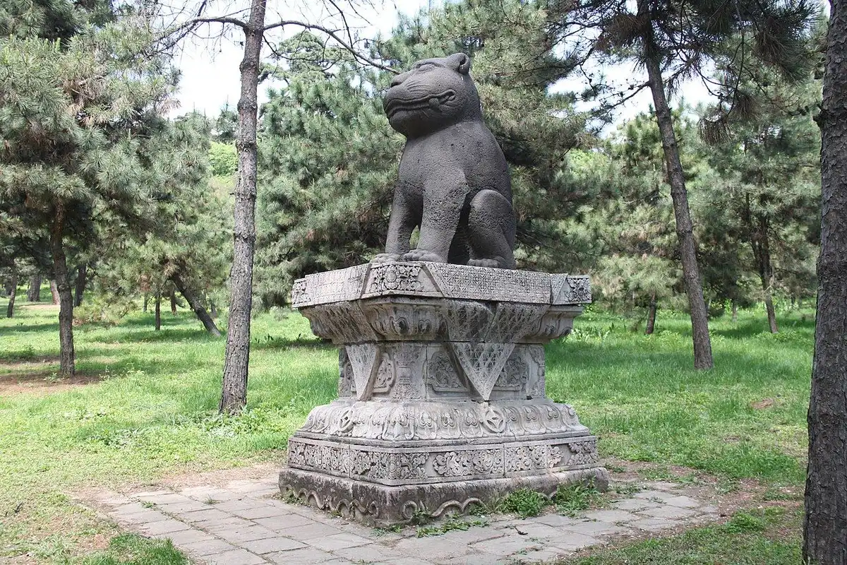 A stone beast on a carved pedestal among pine trees at the Fuling Tomb.