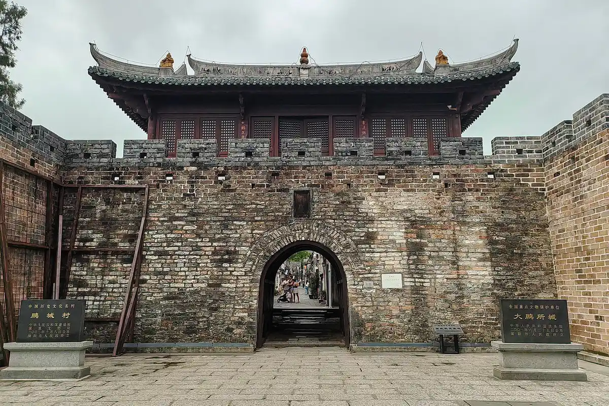 The South Gate of Dapeng Fortress, with a wooden gate tower above old brick walls and an arched gateway.