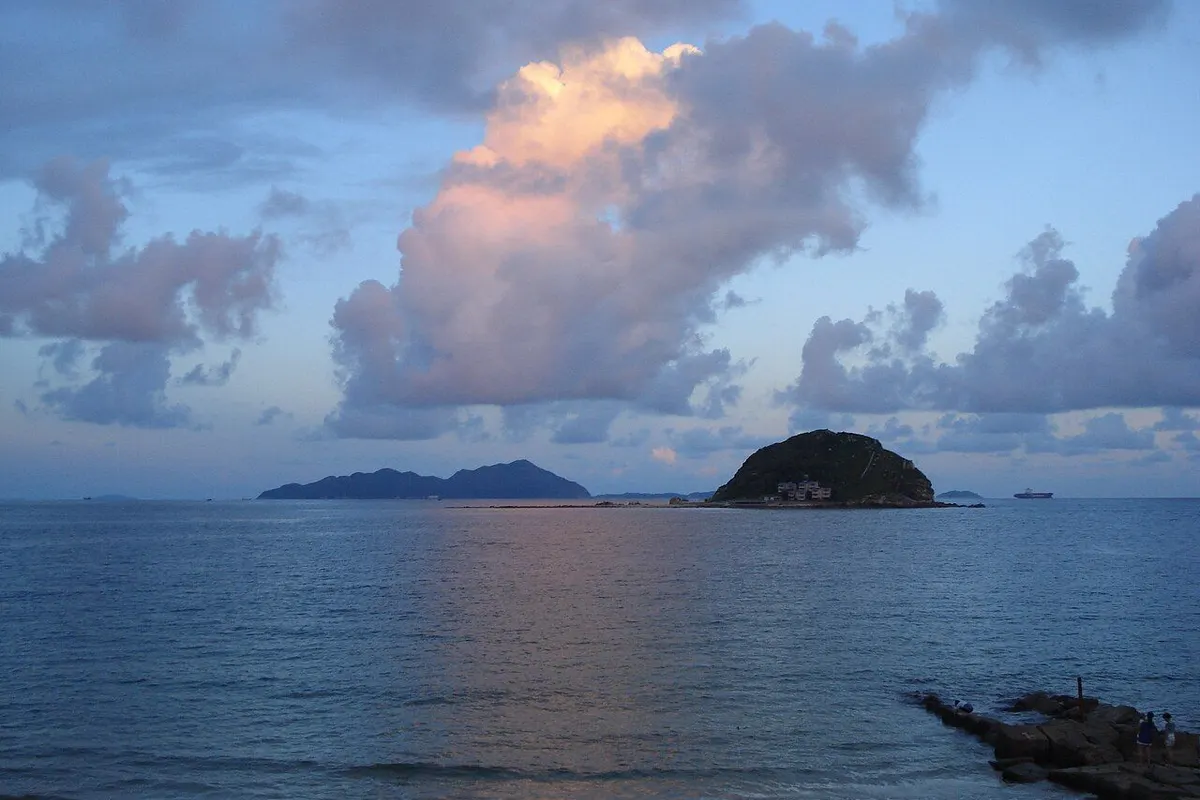 Xichong Beach at dusk, with pink-tinged clouds over a calm sea and a small island offshore.