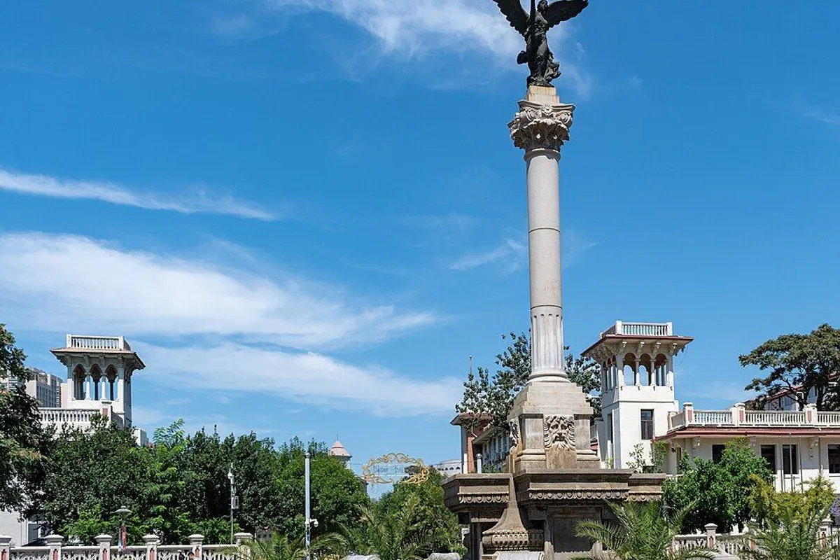 Marco Polo Square with its column and Italian-style villas under a blue sky.