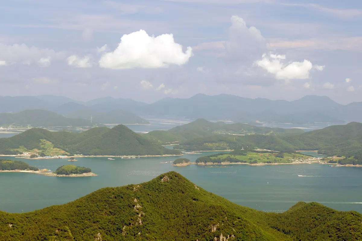 Green islands of all sizes scattered across a blue sea, seen over a forested ridge.