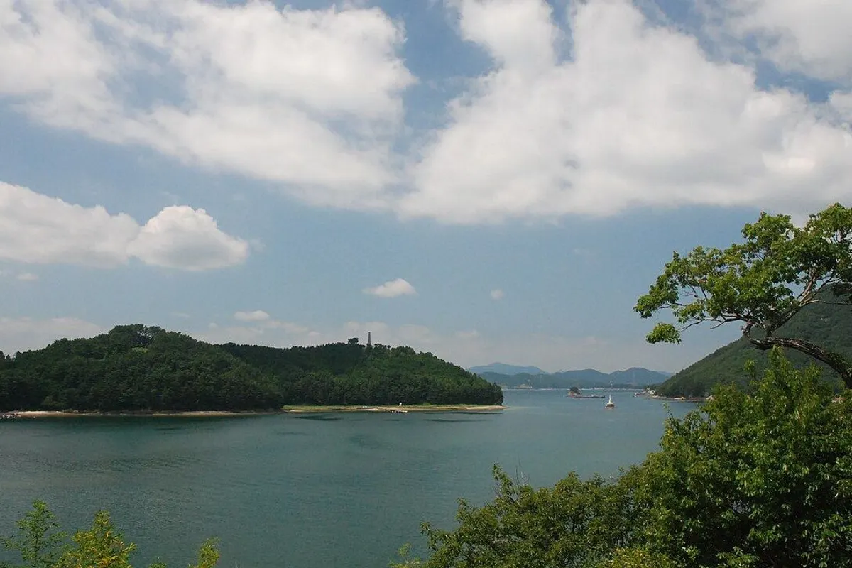 A wooded headland and calm bay on Hansando under summer clouds.