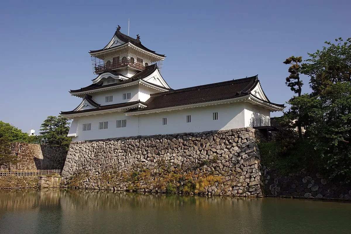 The keep and stone walls of Toyama Castle reflected in the moat under a clear sky.